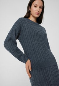 Granatowy sweter robiony na drutach z teksturowanym wzorem prążkowym, okrągłym dekoltem i długimi rękawami, w zestawie z dopasowaną spódnicą.