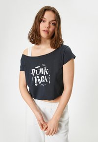Zwarte cropped t-shirt met een losse pasvorm en off-shoulder ontwerp, voorzien van een witte "PUNK" grafische print en korte mouwen. Zachte stoftextuur.