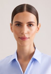 Camicia celeste con colletto, dalla texture liscia, vestibilità sagomata e design classico. Aspetto della pelle chiaro e trucco neutro completano il look.