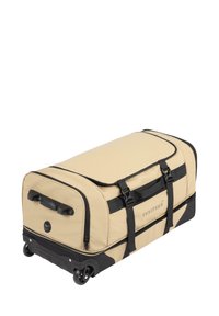 Beige Rolltasche mit schwarzen Akzenten, ausgestattet mit zwei Seitengriffen, einem oberen Reißverschluss und verstellbaren Gurten. Glatte Stoffoberfläche.