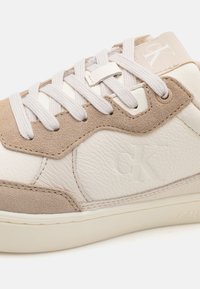 Adidași din piele albă cu accente din suede bej, suprafață texturată, șireturi plate și detaliu cu logo embosat pe lateral.