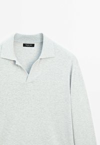 Jasnoszara koszulka polo z miękkiego materiału. Posiada dekolt w serek i krótki kołnierzyk. Subtelna faktura z minimalnymi detalami szwów.