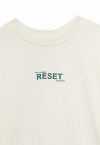 Krémové tričko s krátkým rukávem a žebrovaným kulatým výstřihem. Obsahuje potisk s textem: "CHILL MODE RESET Hra končí" v zelené barvě.