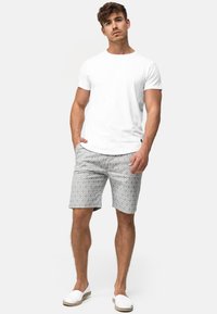 T-shirt blanc à manches courtes, short gris à motifs avec un design en losanges et espadrilles blanches. Tenue simple et décontractée avec deux poches.
