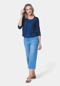 Marinebluse mit Dreiviertelärmeln und Falten; hellblaue, kurze Denim-Jeans; graue Ballerinas mit Schleifenakzent.