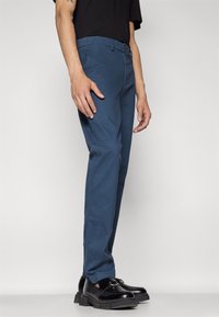 Pantalon en coton bleu à coupe droite, poches latérales et taille boutonnée. Associé à des mocassins en cuir noir.