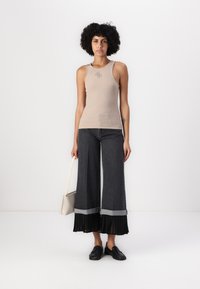 Beige ribbet tanktop med en liten logo, kombinert med mørke vide bukser som har en plissert svart stoffdetalj nederst.