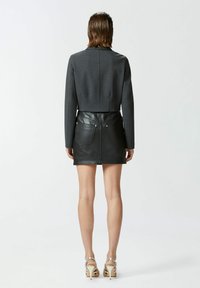 Blazer grigio tagliato con design strutturato e maniche lunghe, abbinato a una mini gonna di pelle nera con tasche posteriori e dettagli in argento.