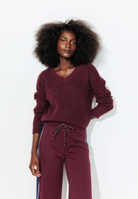 Pull en tricot bordeaux avec un col en V et une texture côtelée, associé à un pantalon ample assorti avec des rayures latérales et une taille à cordon.