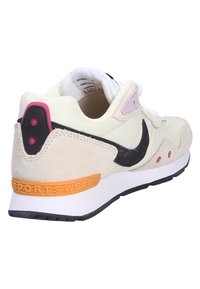 Baskets beige clair en matériaux suédine et maille, avec des accents noirs, un détail rose au talon, et une semelle blanche. Présente "SPORTS WEAR" sur le talon.