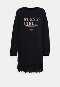 Svart sweatshirtklänning med texten "STUNT GIRL." och stjärngrafik. Har en plisserad svart kjol nedtill, långa ärmar och en rund halsringning.