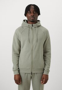 Lys grøn zip-up hoodie lavet af blødt materiale. Har hætte, raglanærmer og ribbede манchetter. Bemærkelsesværdig minimal branding på brystet.