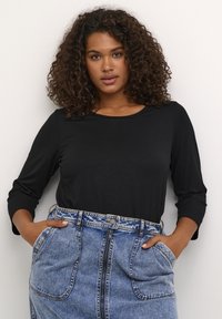 Haut noir à manches longues avec un col rond, associé à une jupe en denim taille haute, dotée d'une fermeture éclair sur le devant et de poches latérales.
