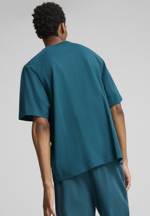 Camiseta suelta de color teal, hecha de algodón suave. Presenta mangas cortas, un escote redondo y un dobladillo recto, combinada con pantalones a juego.