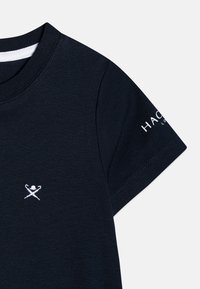 Tummansininen puuvillapaita, jossa on pyöreä kaula-aukko ja lyhyet hihat. Rinnassa on valkoinen brodeerattu logo ja hihassa teksti.