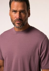 T-shirt di cotone viola con collo a giro e maniche corte, caratterizzato da una texture liscia e un design minimalista, esposto su uno sfondo neutro.