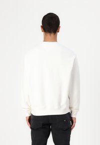 Witte sweatshirt met een ronde hals en geribbelde manchetten, gecombineerd met zwarte jeans. Zachte textuur en een relaxte pasvorm, met een minimalistisch design.