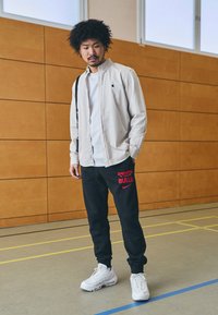 Lys grå skjorte med knapper over en hvit t-skjorte, kombinert med svarte joggebukser med røde "BULLS"-tekster. Hvite joggesko fullfører antrekket.