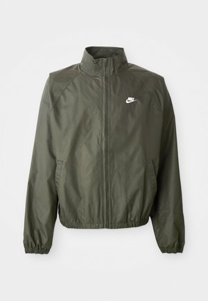Giacca Nike verde oliva con colletto alto, zip frontale, polsini elasticizzati e un piccolo logo bianco sul lato sinistro del petto. Leggera, con texture liscia.