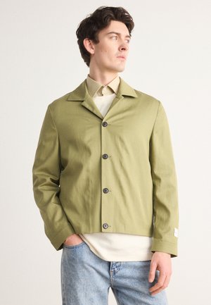 Olive green lightweight jacket with a notch collar, five black buttons, and a relaxed fit, worn over a beige shirt with visible cuffs.