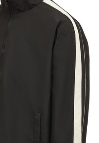 Sort jakke med hvide striber langs ærmerne, en lynlås fortil, en høj krave og en lodret lomme på venstre side.