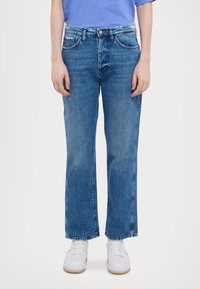 Vaaleansiniset suorat farkut, joissa on hienovarainen kuluminen, viisi taskua ja napillinen vyötärö, yhdistettynä valkoisiin tennareihin.