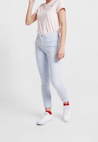 Jeans in denim blu chiaro con vestibilità slim, abbinati a una t-shirt rosa pallido e scarpe da ginnastica bianche con accenti rossi. Dettagli di stile standard.