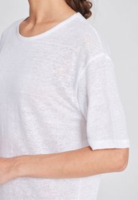 T-shirt bianco semi-trasparente con colletto rotondo e maniche corte, caratterizzata da una texture morbida e leggera e una vestibilità rilassata.