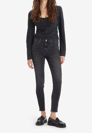 Top de denim negro con mangas largas y escote cuadrado, combinado con jeans negros de cintura alta con dobladillos deshilachados y un corte ajustado.