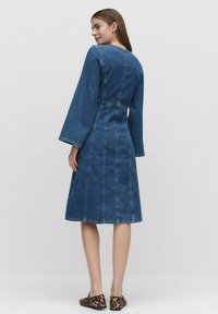 Denim-mekko, jossa on pitkät kelkkamaiset hihat, vyötäröltä kiinteä, polven puoliväliin ulottuva, jossa on pystysuoraan ommeltuja yksityiskohtia, keskipitkä sininen väri.