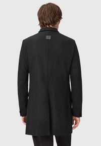 Musta villasekoitetakki, joka on suoran leikkauksen ja yksinkertaisen venttiilin omaava, sekä takana on sävyttävä etiketti. Pitkät hihat, joissa on napitus.