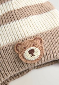 Bonnet tricoté à rayures marron et crème présentant un motif texturé à côtes et un patch rond brodé d'un ours sur le devant.