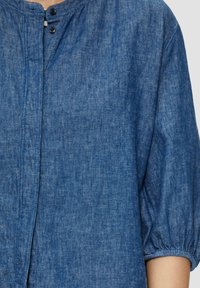 Denim shirt met een ronde halslijn, korte pofmouwen en twee zwarte knopen bij de kraag. Lichtblauwe tint en gestructureerde stof.