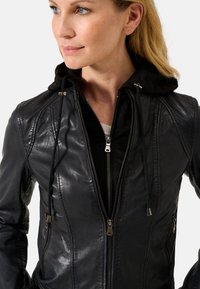 Giacca in pelle nera con chiusura a zip frontale, cappuccio regolabile e dettagli di cucitura sottili. Presenta accessori metallici per la zip e tasche laterali.
