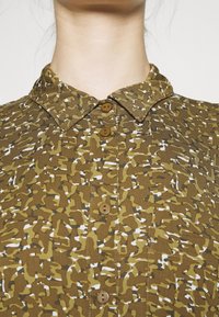 Brun camo-mønsteret skjorte med skjortekrave, der har brune knapper, tekstureret stof og en struktureret pasform.