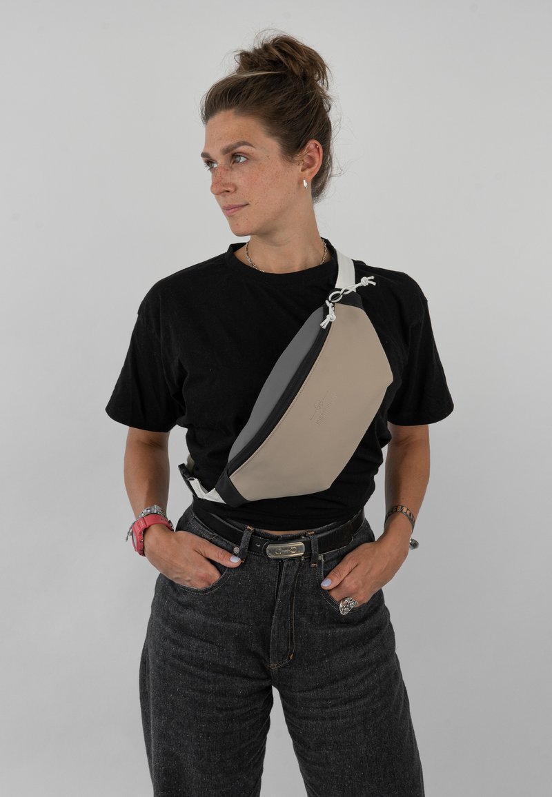 Beige és fekete színű, műanyagból készült, stílusos dizájnnal rendelkező keresztbody táska állítható pánttal és cipzáras záródással.