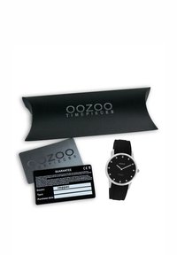 Montre OOZOO noire avec un boîtier rond en argent, un cadran noir, des index horaires blancs, et un bracelet en silicone noir, présentée avec un emballage noir et une carte de garantie.