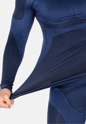Navy blue long-sleeve athletic shirt with textured patterns, stretchy fabric, and fitted design; features contrast stitching and sleek accents.