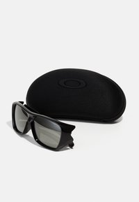 Czarne okulary przeciwsłoneczne z szarymi lustrzanymi soczewkami, charakteryzujące się odważnym, kanciastym wzornictwem. W komplecie z eleganckim, czarnym etui ochronnym.