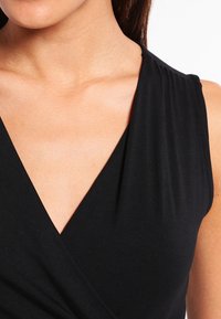 Top senza maniche nero con scollatura a V, caratterizzato da un frontale drappeggiato e un tessuto morbido ed elasticizzato. Texture liscia con dettagli sottili sulle spalle.