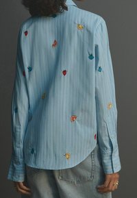 Light blue striped shirt with embroidered fruit motifs in red, green, and yellow. Features a standard collar and buttoned cuffs.