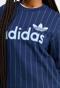 Navy blue sweatshirt featuring thin white vertical stripes, prominent white "adidas" logo, and classic trefoil design on the chest.