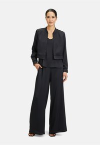 Zwarte, zijden twee-delige outfit bestaande uit een cropped jacket en wijde broek. De jas heeft een ronde halslijn en ribgebreide manchetten.