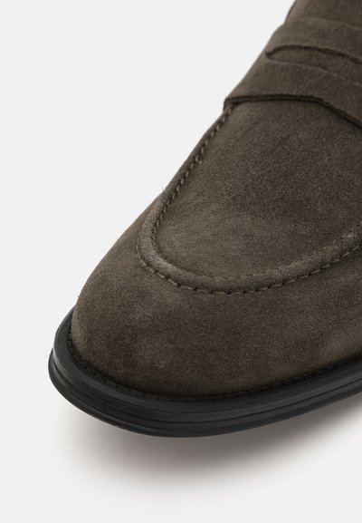 Los mocasines de ante en gris oscuro presentan una punta redondeada, detalle de costura lateral y una duradera suela de goma negra. La textura suave complementa el diseño.