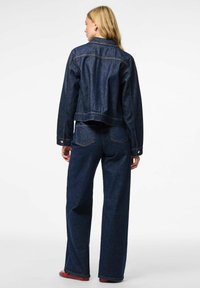 Tamno plava traper jakna s skraćenim dizajnom, oštrim ovratnikom i dugmićima, u kombinaciji s širokim trapericama u istom tonu.