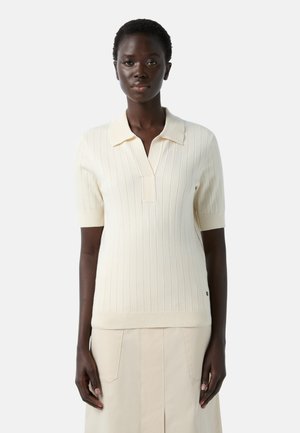 Knit polo sweater in off-white with short sleeves, vertical ribbing, a v-neck, and a small collar. Smooth texture and fitted design.