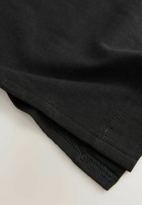 T-shirt en coton noir montrant des bords de tissu repliés avec des détails de couture visibles. Texture douce, surface lisse et design sobre.