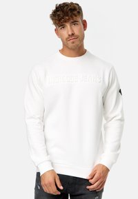 Witte sweatshirt van zacht materiaal, met een gestructureerd logo "INDICODE JEANS" op de borst en ribbelmanchetten en onderrand.