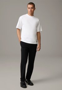 Weißes T-Shirt mit kurzen Ärmeln und Rundhalsausschnitt, kombiniert mit schwarzen Cargo-Hosen mit seitlichen Taschen und dunklen Lederstiefeln. Schlichtes, texturiertes Gewebe.