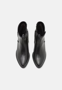 Bottines en cuir noir avec un bout pointu, fermeture éclair sur le côté et texture lisse. Design minimaliste sans embellissements supplémentaires.
